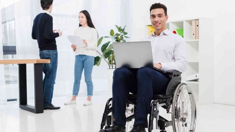 disabled-smiling-young-businessman-sitting-wheelchair-with-laptop-front-business-colleague