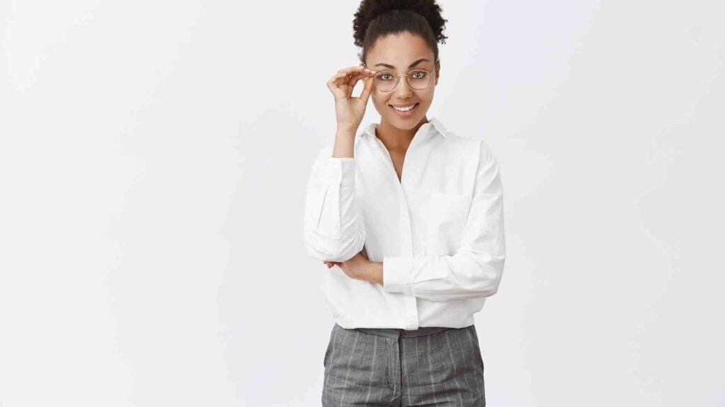 good-looking-stylish-smart-female-psychologist-with-dark-skin-white-collar-shirt-pants-touching-glasses-smiling-with-self-assured-expression-gazing