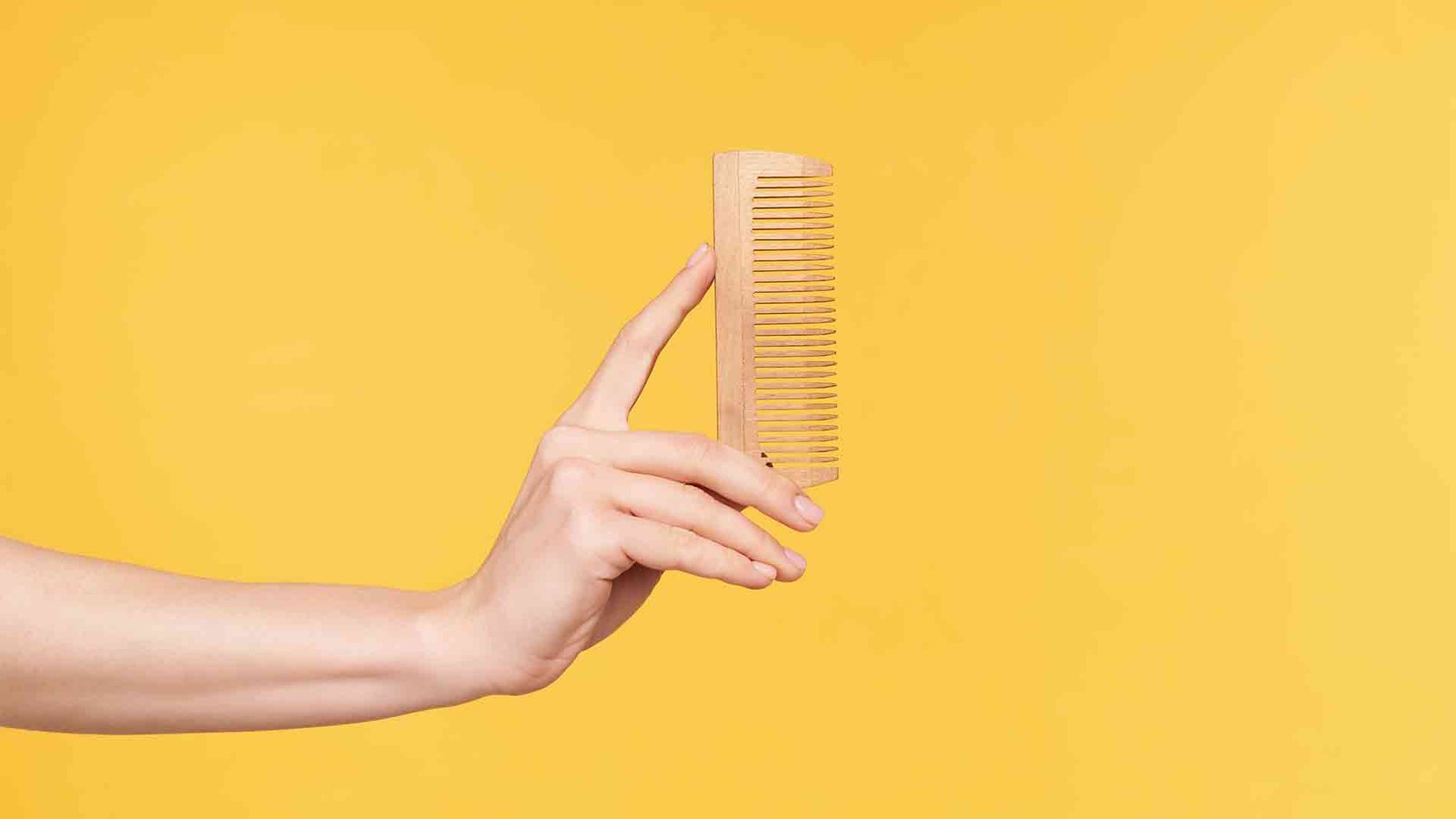 side-view-young-well-groomed-woman-s-hands-keeping-upright-wooden-while-going-comb-hair-isolated-orange-background-haircare-human-hands-concept