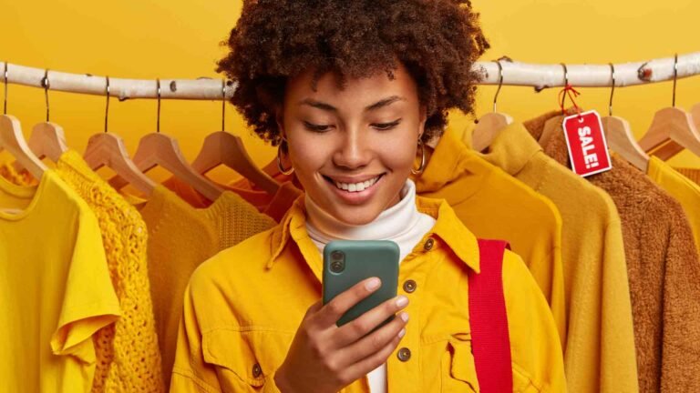 glad-online-merchant-focused-smartphone-device-stands-against-yellow-clothing-racks