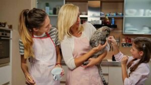 blonde-female-holds-cat-two-teenage-girl-cooking-kitchen