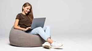 happy-young-woman-sitting-floor-using-laptop-gray-wall