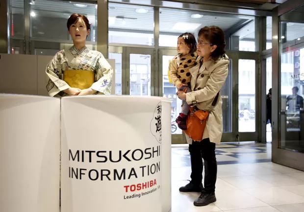 Visitantes olham robô recepcionista em loja em Tóquio nesta segunda-feira (20) (Foto Issei Kato Reuters)